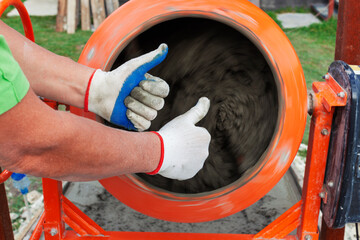 Two male hands with a gesture of approval against the background of a working concrete mixer