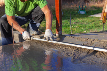 Improvement of the yard, a man evens out the concrete solution on the path with the ruleб close-up