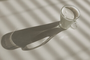 Glass mug with kefir on white dining table, natural light