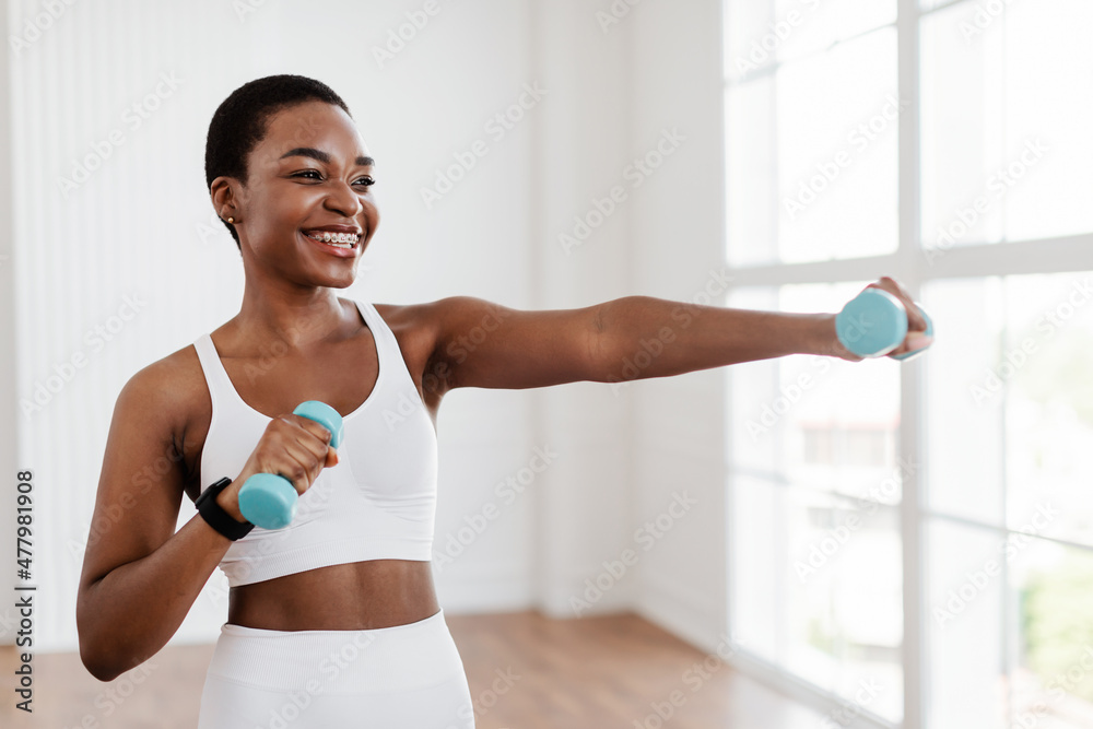 Wall mural Afro Sporty Woman Exercising With Two Dumbbells And Posing