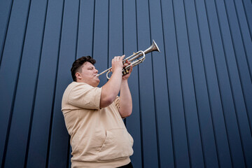 Young street musician playing the trumpet near the big blue wall