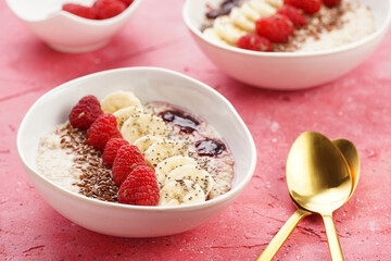 trendy breakfast bowl with oatmeal porridge, fresh raspberries, banana, chia seeds, linseed and jam on magenta surface