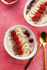 trendy breakfast bowl with oatmeal porridge, fresh raspberries, banana, chia seeds, linseed and jam on magenta surface