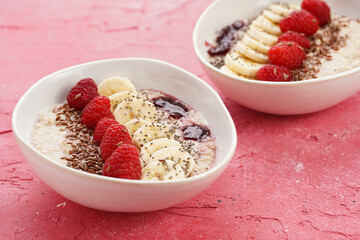 trendy breakfast bowl with oatmeal porridge, fresh raspberries, banana, chia seeds, linseed and jam on magenta surface