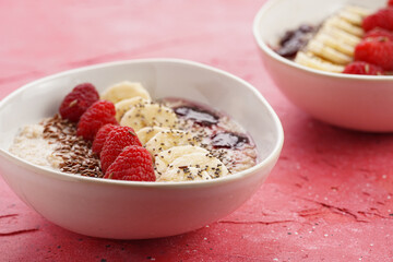 trendy breakfast bowl with oatmeal porridge, fresh raspberries, banana, chia seeds, linseed and jam on magenta surface