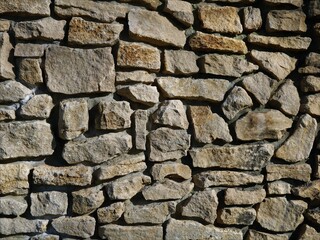 fragment of a stone wall with a rough texture of large masonry from natural rough cobblestones, solid stone texture in bright sunlight with detailing broken lines and chaotic irregularities