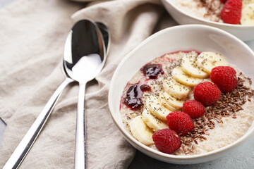 Trendy breakfast bowl with oatmeal porridge, fresh raspberries, banana, chia seeds, linseed and jam