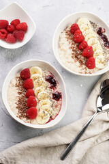 Trendy breakfast bowl with oatmeal porridge, fresh raspberries, banana, chia seeds, linseed and jam