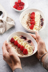 Male hands holding a trendy breakfast bowl with oatmeal porridge, fresh raspberries, banana, chia seeds, linseed and jam
