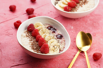 trendy breakfast bowl with oatmeal porridge, fresh raspberries, banana, chia seeds, linseed and jam on magenta surface