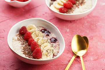 trendy breakfast bowl with oatmeal porridge, fresh raspberries, banana, chia seeds, linseed and jam on magenta surface