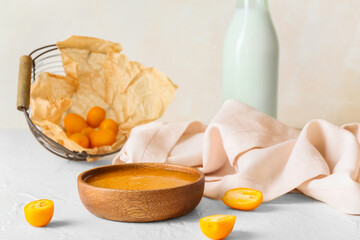Bowl of tasty kumquat jam and cut fresh fruits on light background