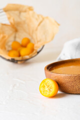 Bowl of tasty kumquat jam and cut fresh fruits on light background, closeup