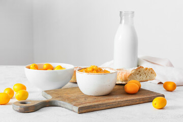Bowl of tasty kumquat jam and fresh fruits on light background