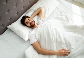 Fototapeta Arab guy sleeping resting peacefully in his comfortable bed at home, lying with closed eyes, above view obraz
