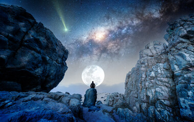 person on the rock outdoors meditating or praying at night under the Milky Way and Moon, back view
