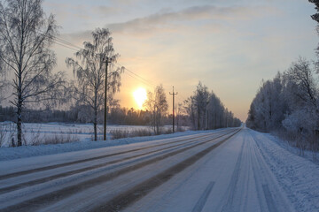 Winter road on a frosty day. Beautiful landscape with the sun in the haze and the trees in the snow