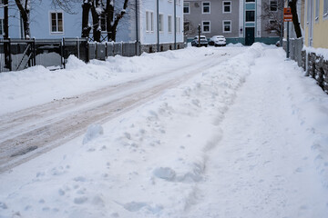 Slippery snowy city road  during winter. Difficult weather conditions. Street and sidewalk under snow piles. Dangerous traffic.