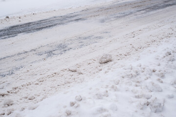 Slippery snowy city road  during winter. Difficult weather conditions. Street and sidewalk under snow piles. Dangerous traffic.