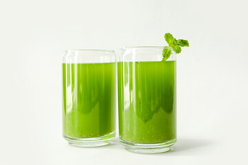 Glasses of green juice with mint leaves on light background