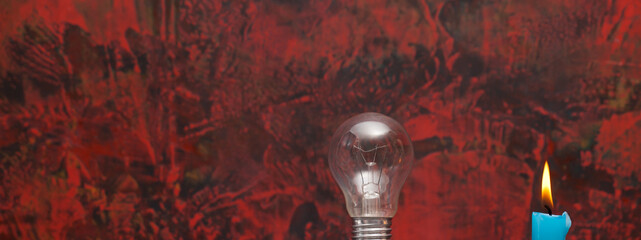 Light bulb and lit blue candle on an abstract red and black background.