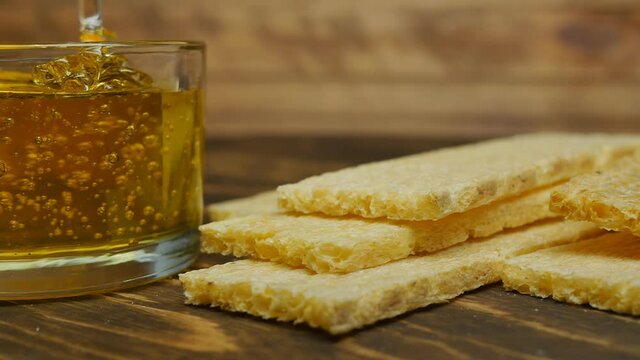 fresh thick fragrant honey is poured in a trickle into a glass cup and bread slices lie on a wooden table. Dolly movement. Close-up
