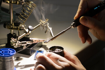 Smoke from a soldering iron and a hand holding a modern thermoregulated soldering iron. Dark tones,...