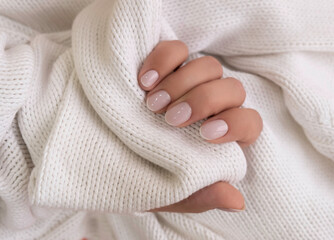 Well-groomed female hands, delicate manicure on a white knitted background, close-up