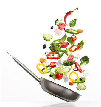 Fresh vegetables flying into pan, isolated on white background