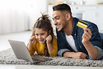 Dad And Little Daughter With Laptop And Credit Card Making Online Shopping