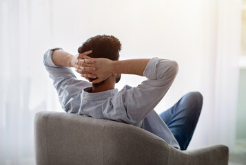 Lazy day. Relaxed guy resting on comfortable armchair, holding hands behind head, enjoying silence,...