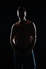 Silhouette picture of a hot shirtless muscular man posing in jeans in a dark studio.