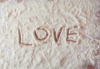 Love written with finger on a flour spread over a kitchen table.