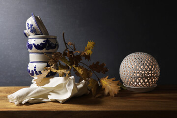 Natura morta con vaso bianco e blu in ceramica, foglie di quercia e candela su fondo scuro © Enzo Pancaldi