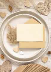 Wedding table place with blank card and envelope near dried plants and hearts, mockup