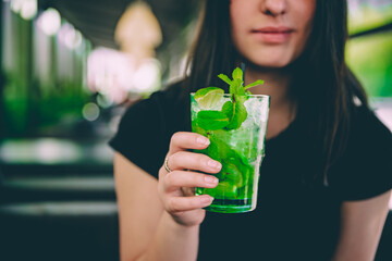 young woman's hand holding a glass with mojito lemonade cocktail in cafe