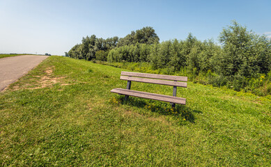 Inviting plastic bench in the grass of the roadside along a narrow country road. The photo was taken on a sunny summer day in the Dutch province of North Brabant.
