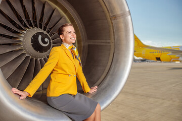 Fototapeta na wymiar Cheerful woman stewardess sitting on aircraft engine