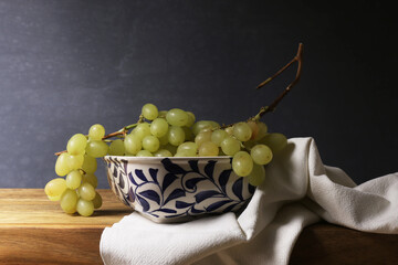 
Natura morta con grappoli d’uva bianca, ciotola in ceramica bianca e blu, tessuto di lino, isolata su fondo scuro