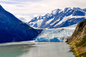 Fototapeta na wymiar Aerial shot of a glacier calving into the water of Prince William Sound, Kenai Peninsula. A stunning snow-capped mountain range in the background and icebergs float in the water below - Alaska