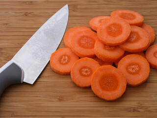 Heap of Orange carrot slices with knife on a wooden cutting board.