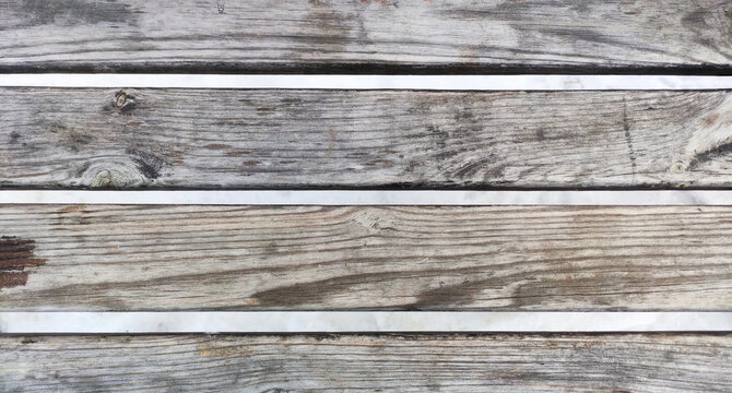 Close-up photo part of a wooden bench that is worn and faded in color a backdrop of snow. Wooden horizontal slats.