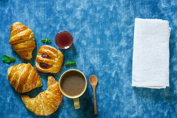  Continental breakfast captured from above (top view, flat lay). Coffee, orange juice, croissants, jam, honey and flowers. Grey stone worktop as background. Layout with free text (copy) space.