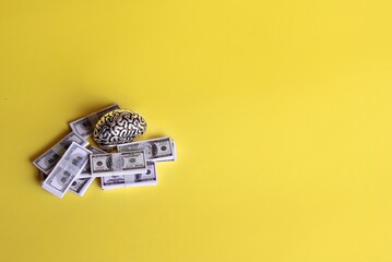 Monetization, knowledge or business minded concept. Brain model and stack of money on yellow background. Copy space for text.