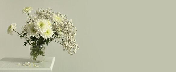 White chrysanthemums and gypsophila  flower in glass on gray interior. Selective soft focus. Minimalist still life. Light and shadow nature horizontal long background.