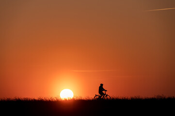 Naklejka na ściany i meble Silhouette of man on bike on grass on sunset with back lite and sun on backgound