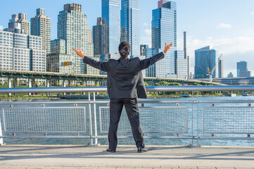 Facing dramatic high buildings of New York City, a middle age businessman is raising both arms, a symbol of success..