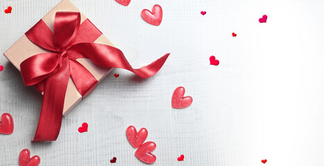 Top view photo of valentine's day decorations white gift box with red ribbon bow and small hearts on isolated light background.