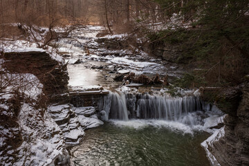 Water from a stream cascades down a small waterfall at Buttermilk Falls State Park in Ithaca, NY during a cold winter day.