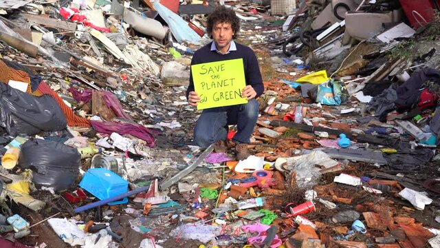 Man  40 years old ecologist holding a sign with the words save the planet go green, protest against climate change, global warming and atmospheric pollution in a garbage dump waste